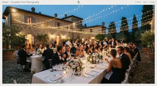 A breathtaking, wide-angle shot of a wedding reception in a historic Italian villa at dusk. Thousands of fairy lights are strung across an open courtyard, reflecting off crystal glasses and silver cutlery on long, elegantly decorated tables. The lighting is warm and golden against the deep blue twilight sky. Guests are seen in blurred motion, creating a lively yet sophisticated atmosphere that feels like a scene from a high-end fashion editorial.